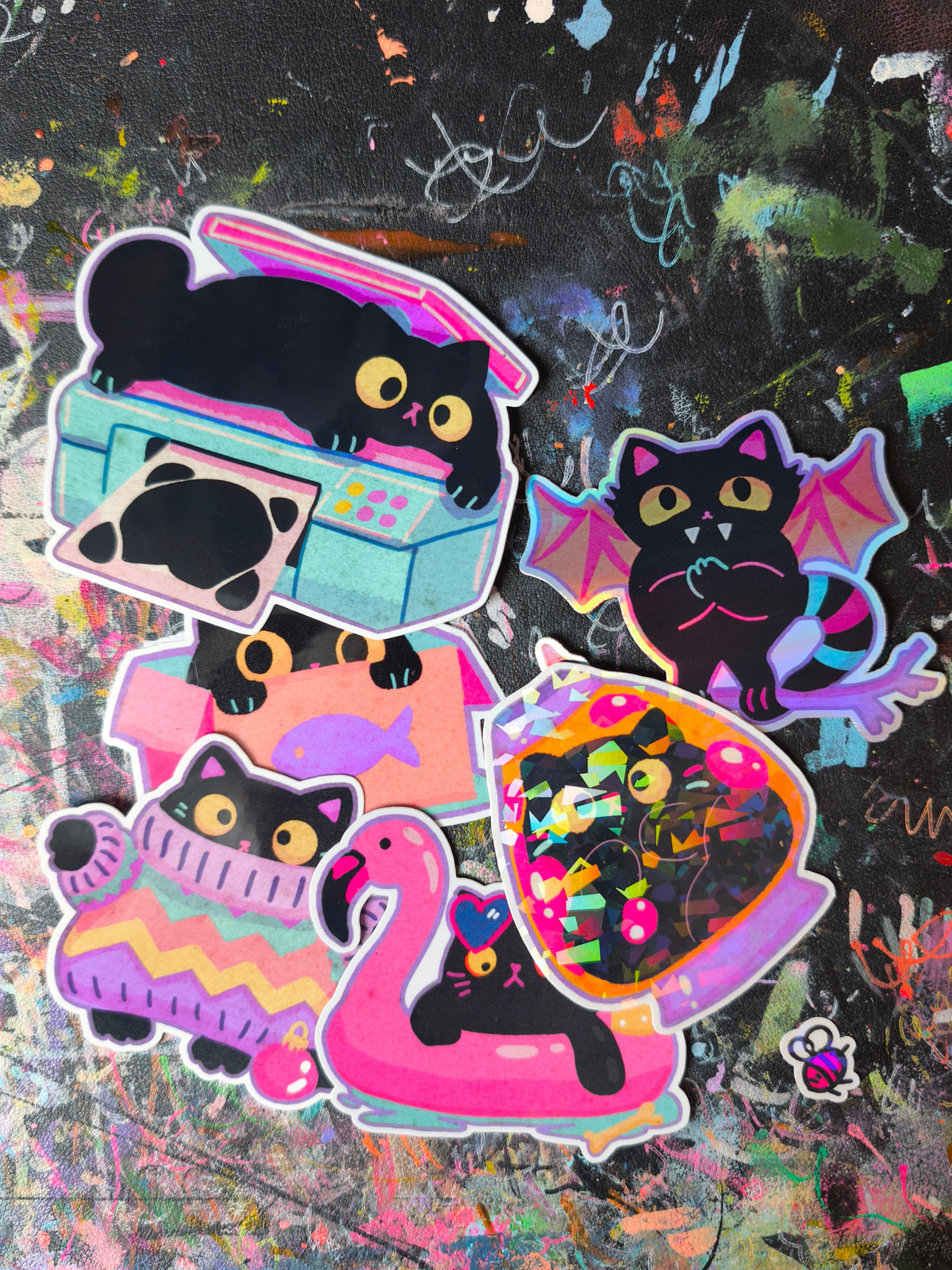 Six handmade black cat stickers in pink, purple and turquoise on the artist's studio table
